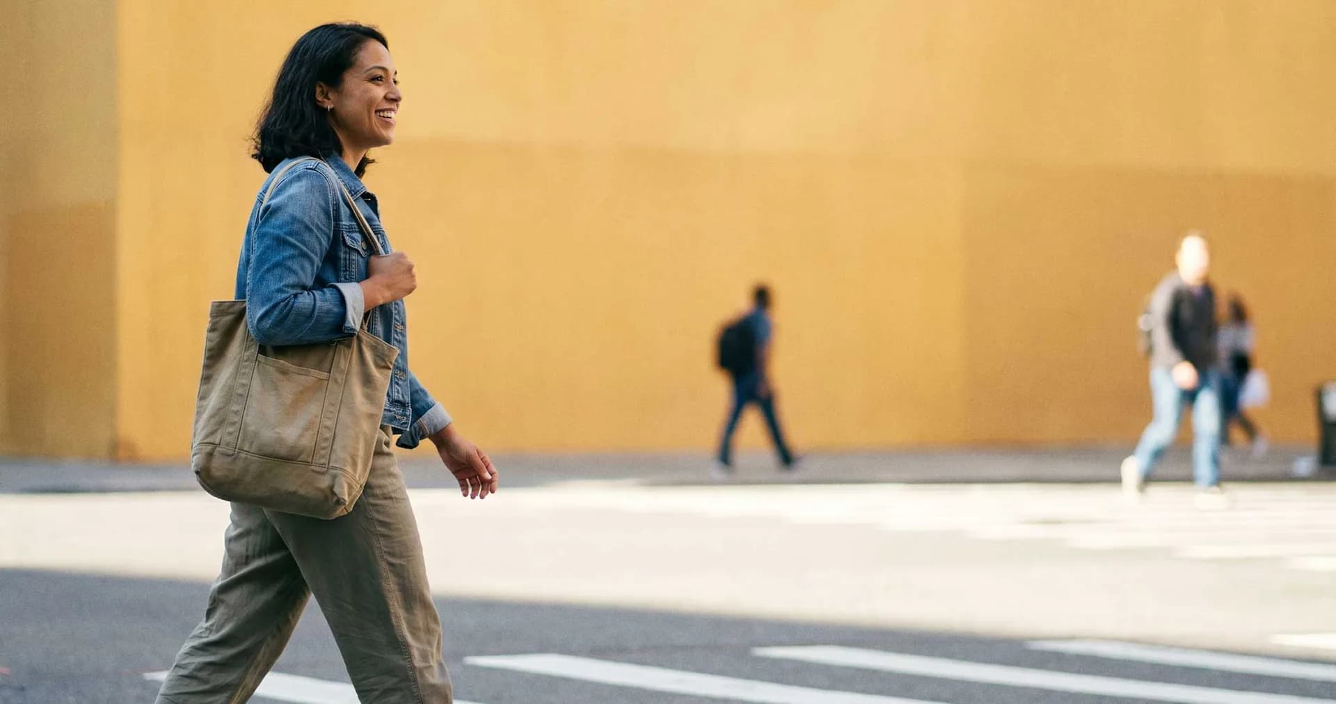 Smiling woman with a tote bag walking across a city street